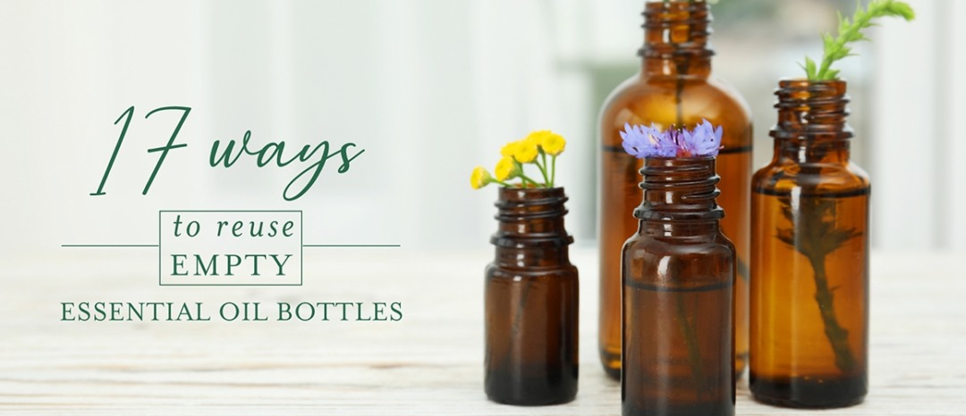 Four empty glass bottles in different sizes decorated with fresh flowers with title "17 Ways to Reuse Empty Essential Oil Bottles" on the image